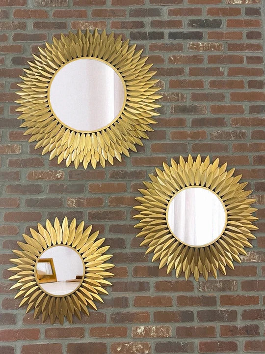 The Broche Mirror with radiating hand-painted antique-gold steel leaves around a round reflective center.