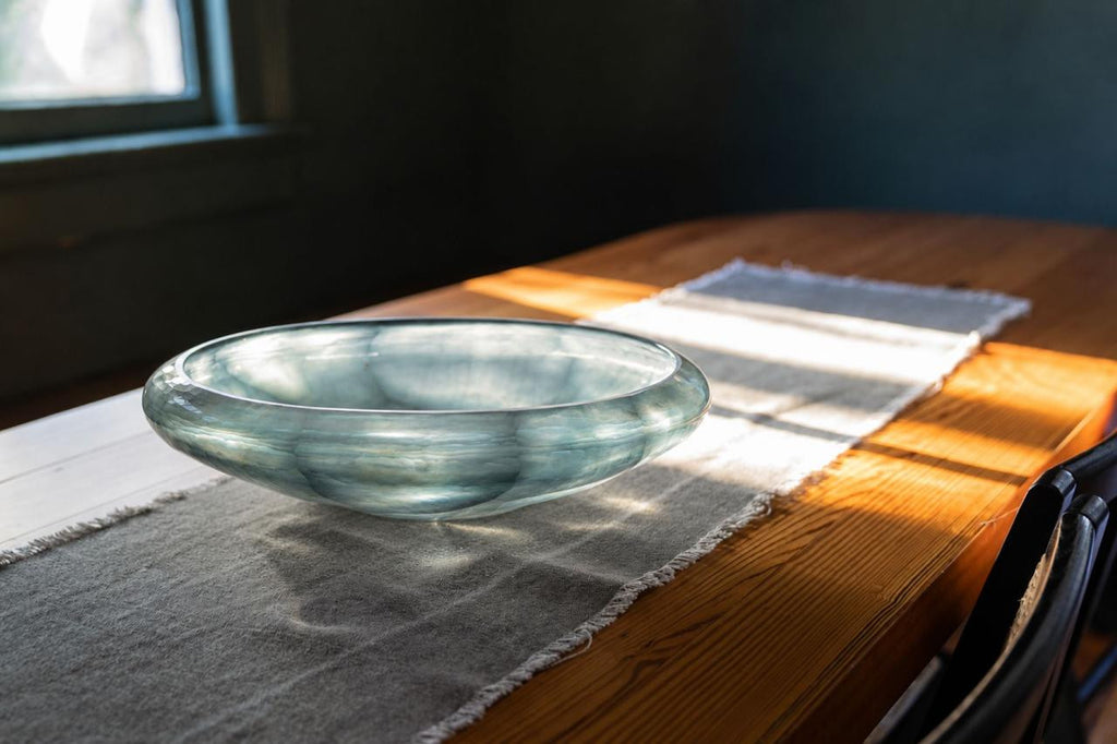 Marine Glass Bowl centered on a wood dining table with sunlight passing through the blue glass.
