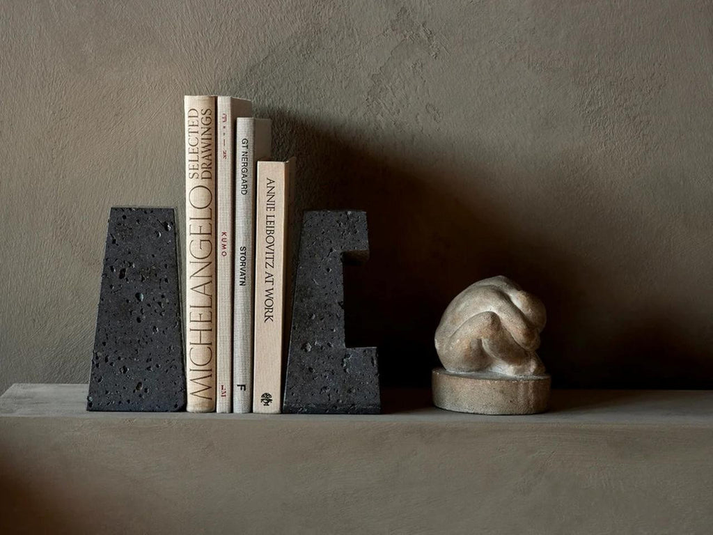 Converge Bookends holding a row of books on a taupe shelf beside a small sculptural object.