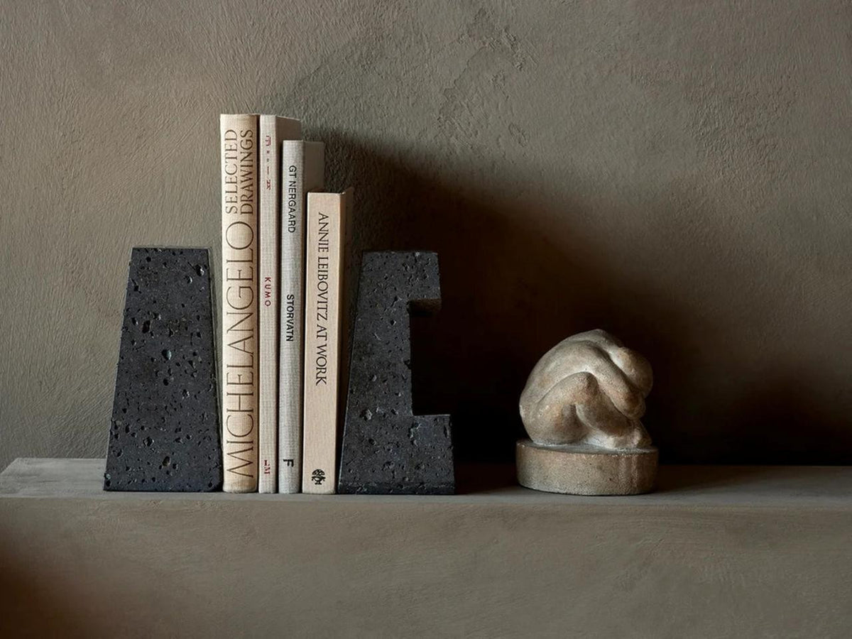 Converge Bookends holding a row of books on a taupe shelf beside a small sculptural object.