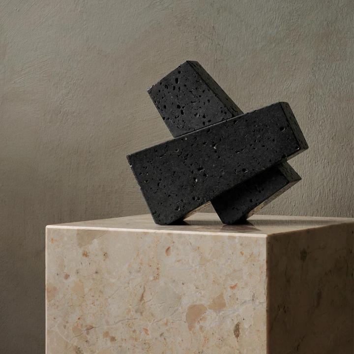 Interlocked Converge Bookends displayed as a black stone sculpture on a pale travertine plinth.