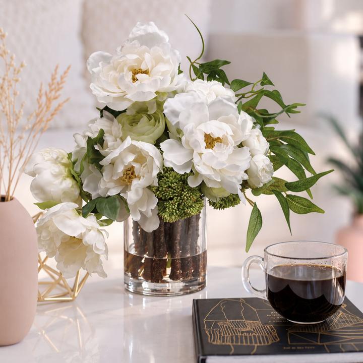 Geneviève floral arrangement displayed on a light table beside a dark glass and decorative book.