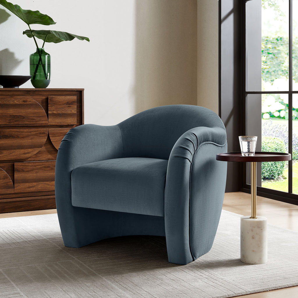 Storm-blue velvet curved armchair placed beside a marble-top side table in a modern living room