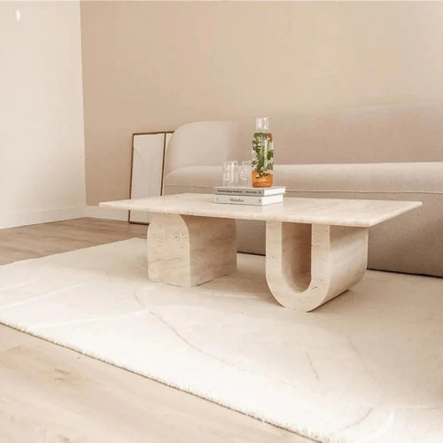 Travertine coffee table showing U-shaped leg and solid rectangular leg against a beige sofa
