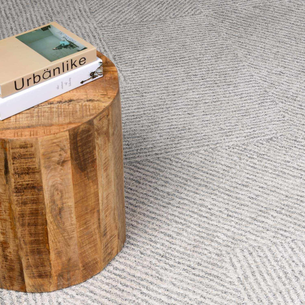 Corner view of ivory diamond-patterned rug beside a round solid wood pedestal side table
