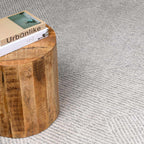 Corner view of ivory diamond-patterned rug beside a round solid wood pedestal side table