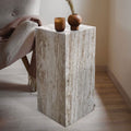Travertine cube side table with natural vein-cut texture styled beside a gray armchair with a vase and candle
