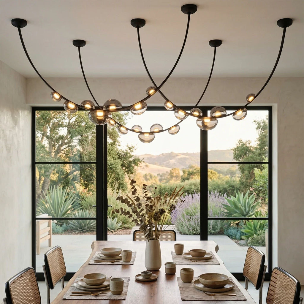 Céline Chandelier three-arc configuration hanging above a long dining table with rattan chairs