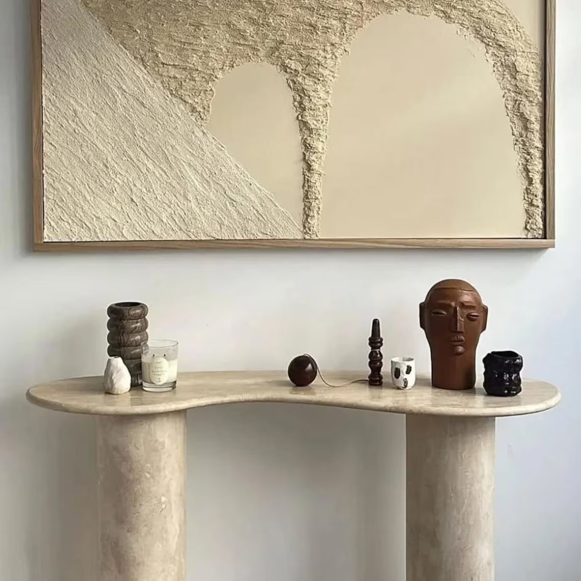 The Céleste Console styled in a hallway beneath framed art, holding a candle and small sculptural objects.