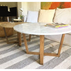 Round marble coffee table with walnut legs in front of a white sofa with magazines on top