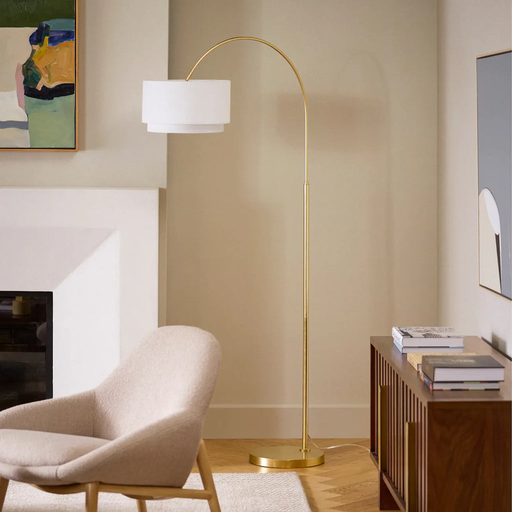 Brass arc floor lamp with linen shade positioned beside a cream armchair and wood console