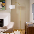 Brass arc floor lamp with linen shade positioned beside a cream armchair and wood console