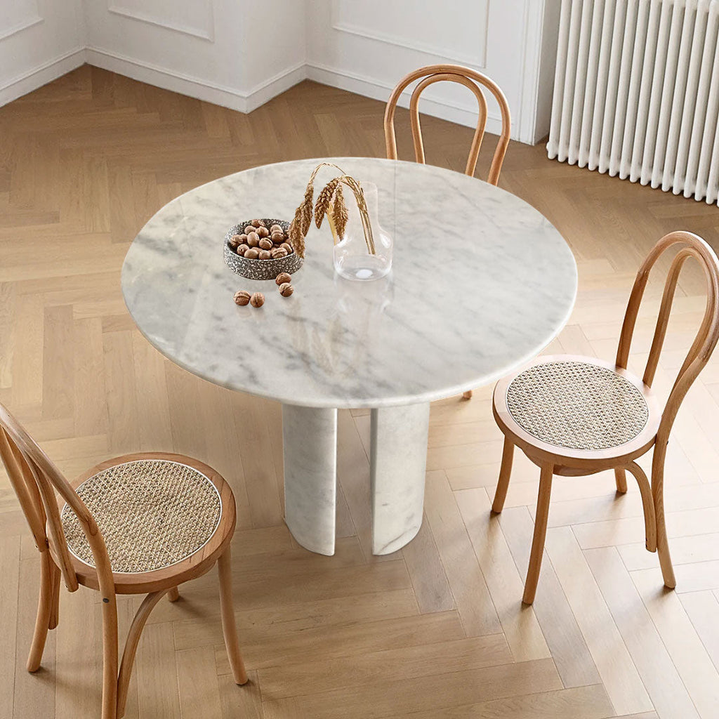 Round white marble dining table with twin curved column legs surrounded by rattan cane chairs