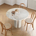 Round white marble dining table with twin curved column legs surrounded by rattan cane chairs