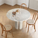 Round white marble dining table with twin curved column legs surrounded by rattan cane chairs