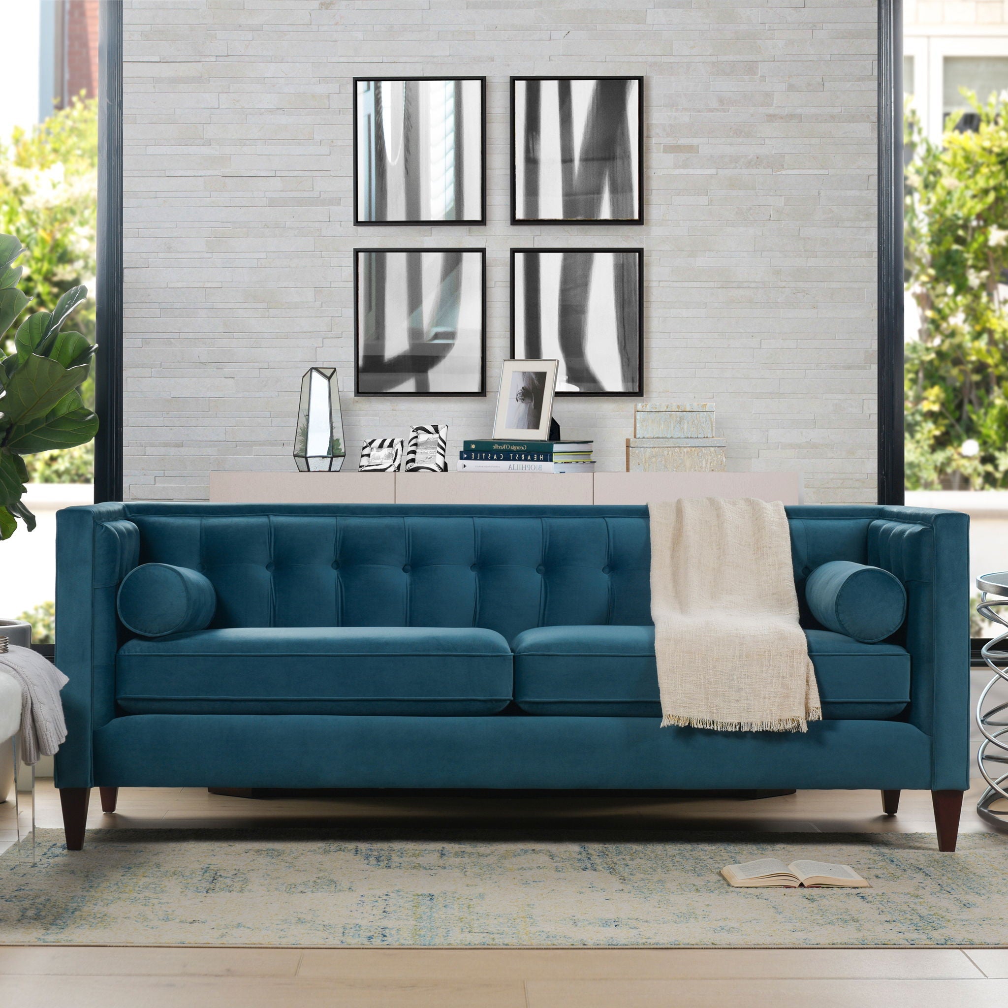 Elegant 84-inch sofa from the Cadence collection featuring a geometric tuxedo silhouette and internal button tufting in rich teal blue. Shown from a straight-on studio view styled with a cream throw blanket against a light brick accent wall.
