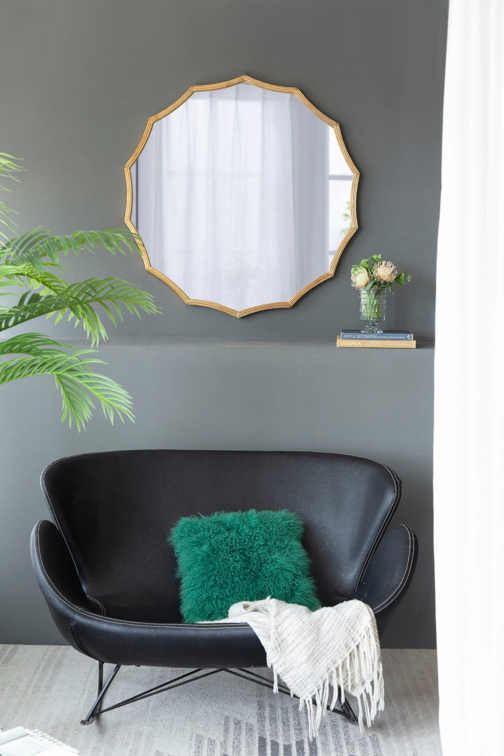 Gold sunburst mirror styled above a black leather loveseat with a green accent pillow