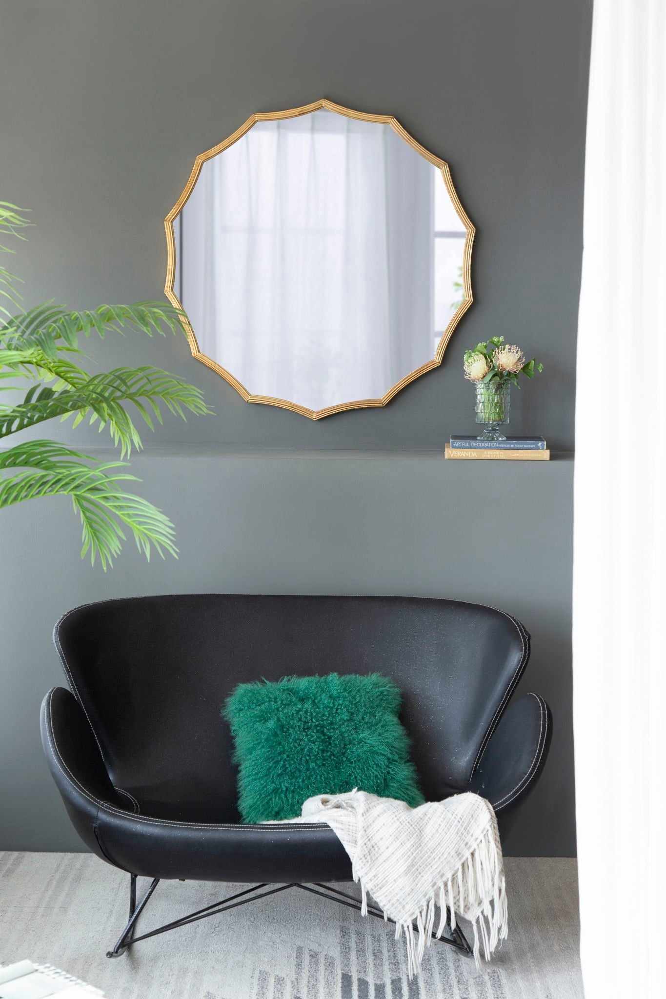 Gold sunburst mirror styled above a black leather loveseat with a green accent pillow