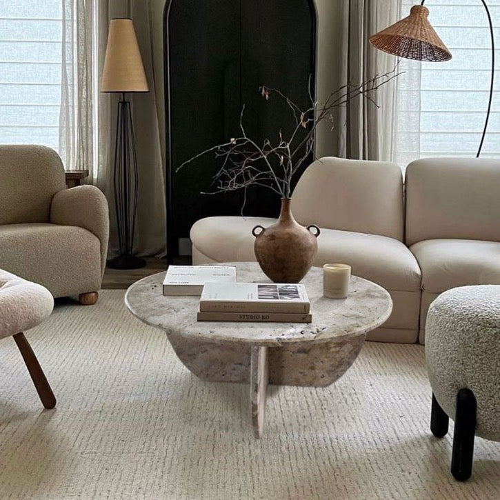 Round travertine coffee table styled in a neutral living room with a woven pendant light