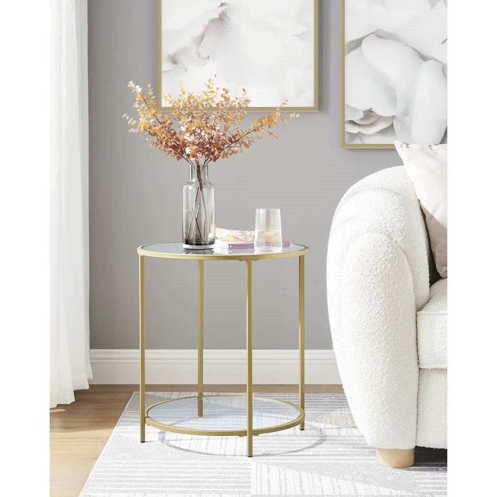 The Joséphine Side Table beside a cream boucle sofa, showing its gold steel frame and glass shelves in a living room setting.