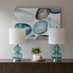 Pair of blue glass table lamps styled on a wood console beneath framed art