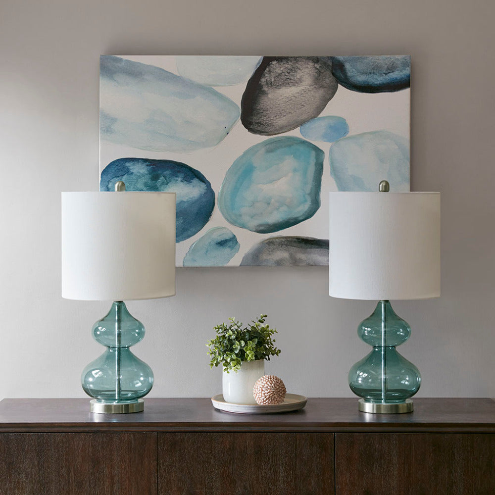 Pair of blue glass table lamps styled on a wood console beneath framed art
