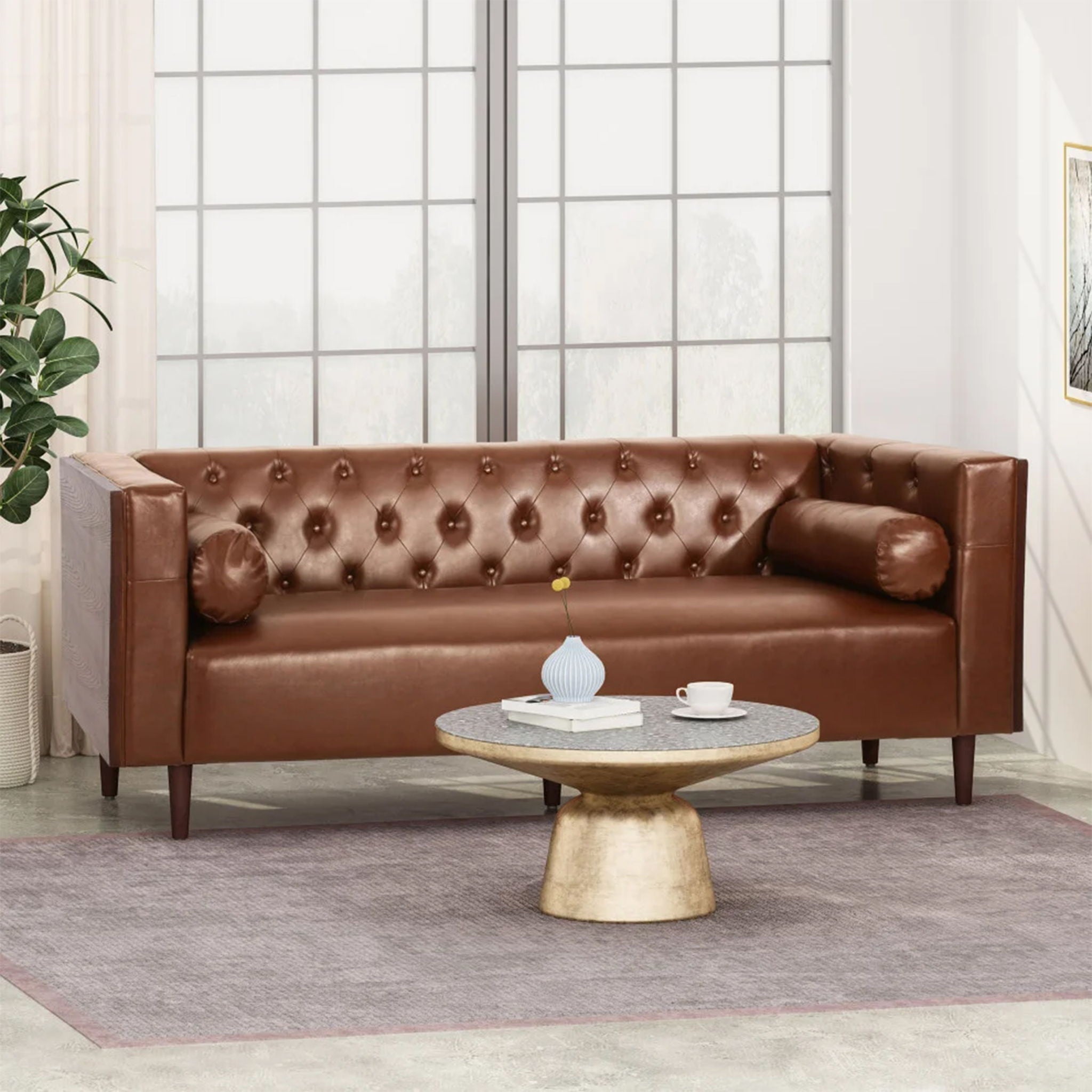 Luxury 90-inch tuxedo sofa from the Monolith collection in premium light brown leather, featuring an interior grid of deep button tufting. Shown in a styled editorial lounge space behind a round gold-based coffee table.