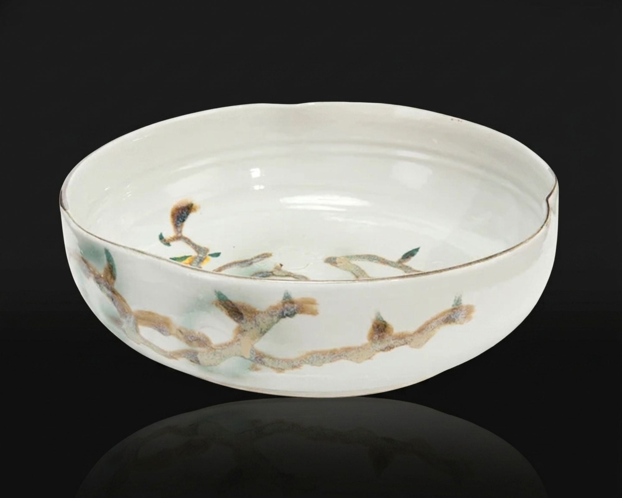 Nadine Bowl in glossy ivory ceramic with a branching botanical motif shown against a dramatic black background with a subtle reflective surface.