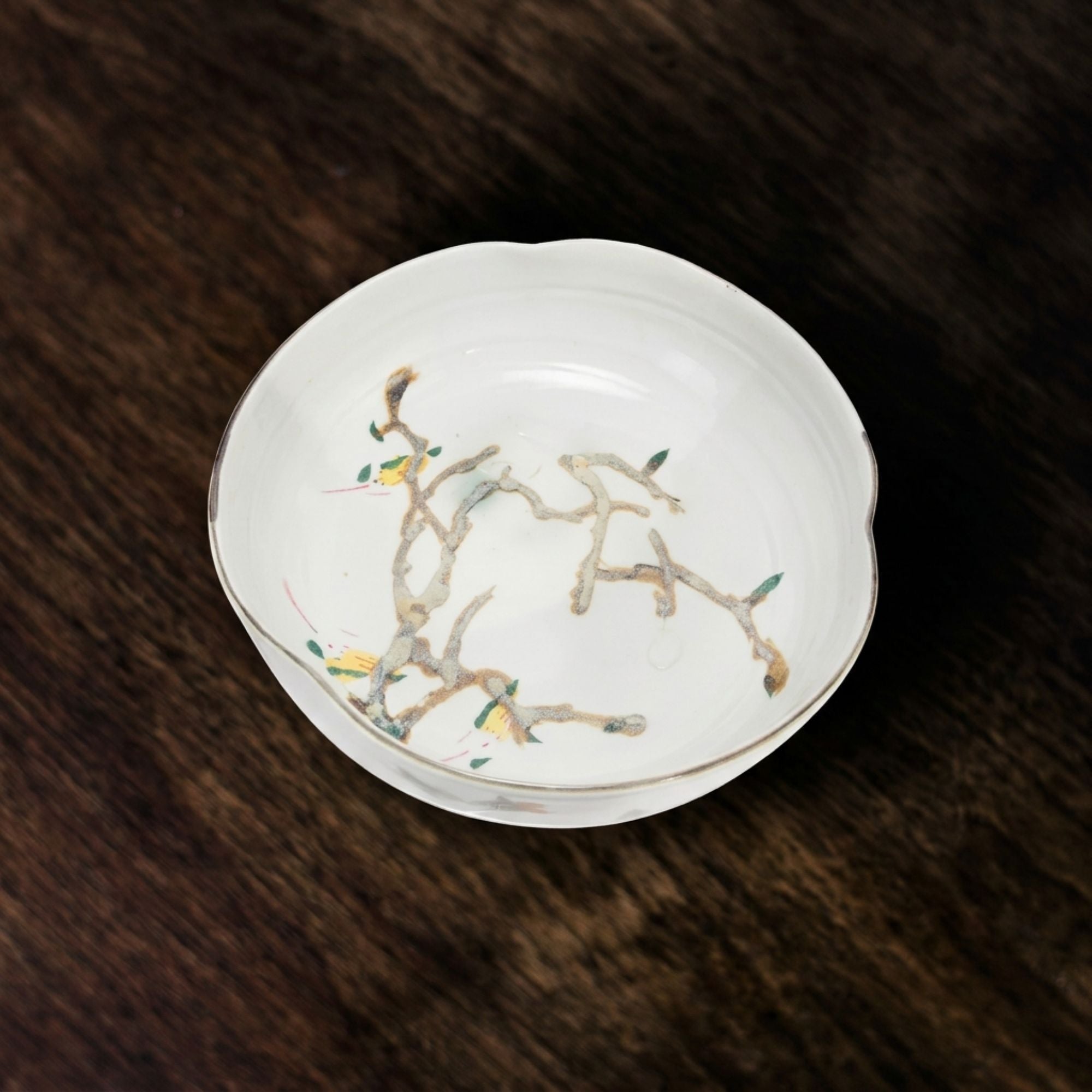 Nadine Bowl viewed from above on a richly grained dark wood tabletop, highlighting its ivory glaze and delicate branching botanical motif.