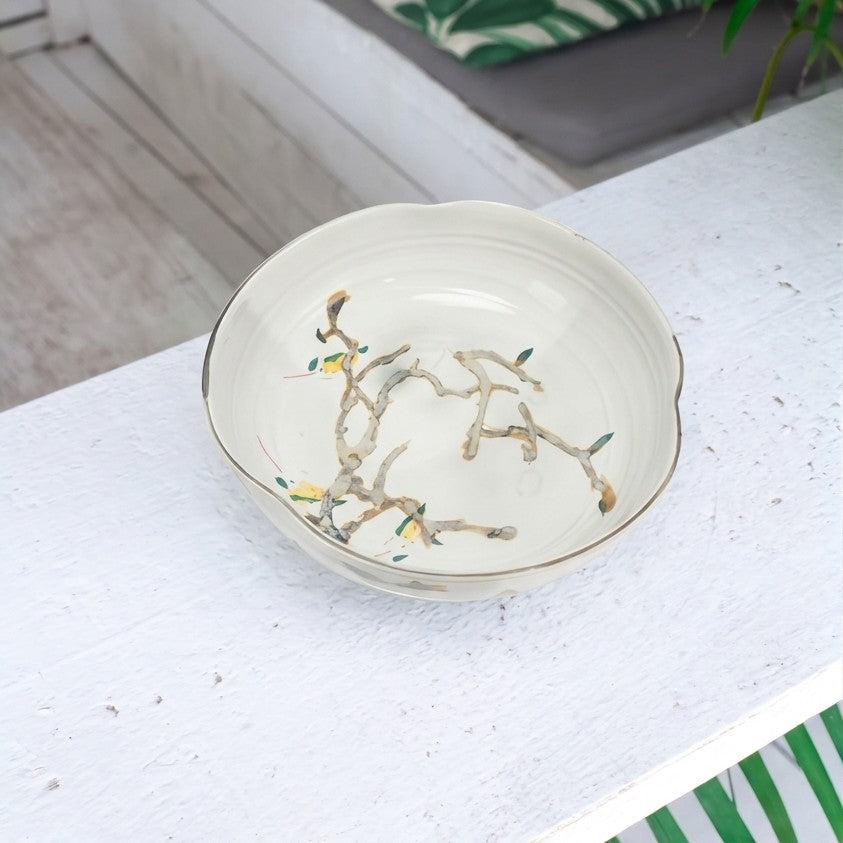 Nadine Bowl displayed on a white painted wood table, showing its ivory ceramic surface and organic branch motif with subtle green and gold accents.
