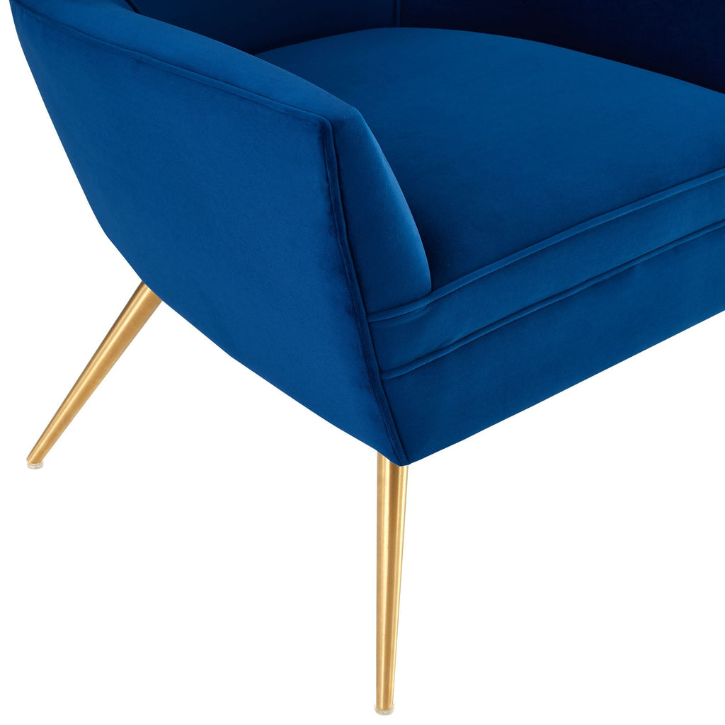 Close-up of the brushed gold splayed legs beneath the Renata Armchair's navy velvet frame