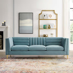Light blue velvet sofa styled beneath a gold shelving unit in a modern living room