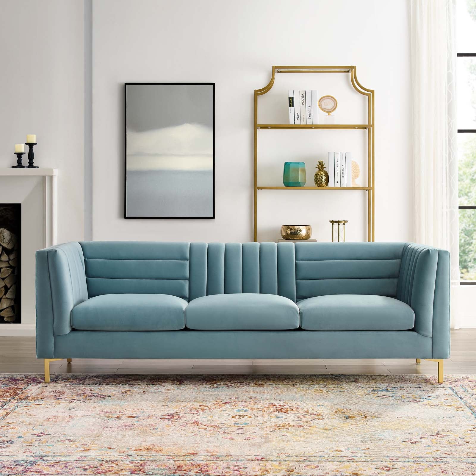 Light blue velvet sofa styled beneath a gold shelving unit in a modern living room
