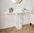 White Carrara marble console table with fluted pedestal base styled with a framed photo and candle beneath a gold mirror