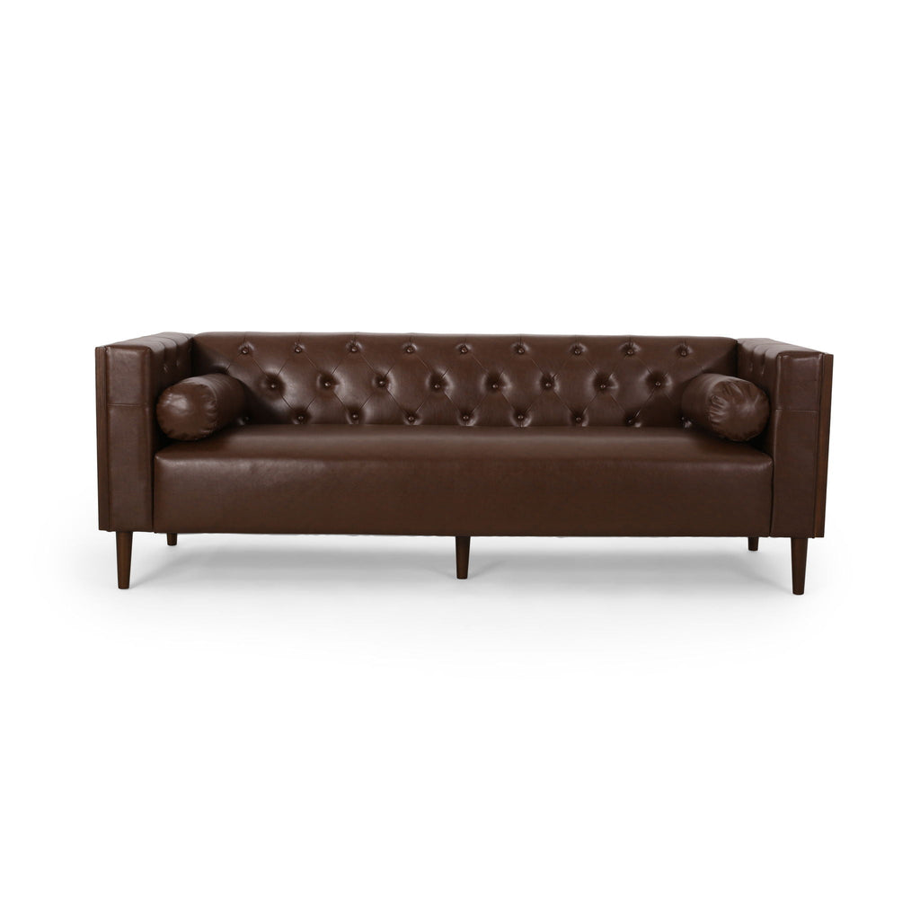 Symmetrical straight-on studio view of the Monolith tuxedo sofa dark brown leather, highlighting the flat bench seat cushion, internal diamond tufting, and cylindrical bolster pillows against a clean white background.