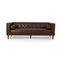 Symmetrical straight-on studio view of the Monolith tuxedo sofa dark brown leather, highlighting the flat bench seat cushion, internal diamond tufting, and cylindrical bolster pillows against a clean white background.