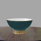 Peacock green and gold porcelain bowl displayed on a wood console against a neutral gray backdrop