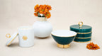 The peacock Arienne Box grouped with an ivory porcelain vase, candle, and matching bowl, styled with fresh orange flowers on a linen surface