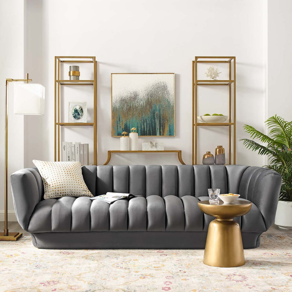 The Cannelé Sofa in charcoal gray velvet styled in a high-end white living room between two symmetrical gold étagère bookshelves.