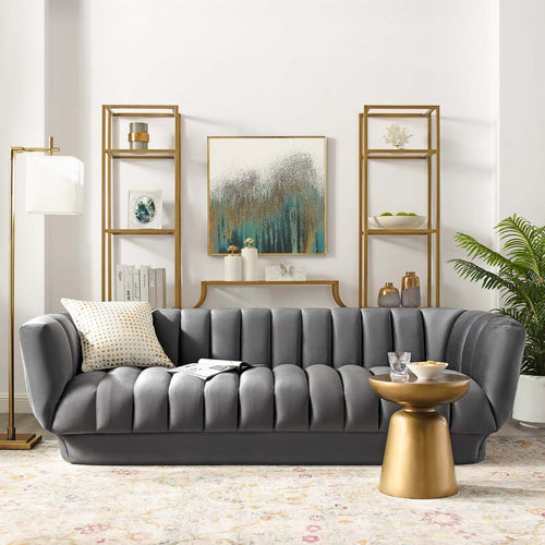 The Cannelé Sofa in charcoal gray velvet styled in a high-end white living room between two symmetrical gold étagère bookshelves.
