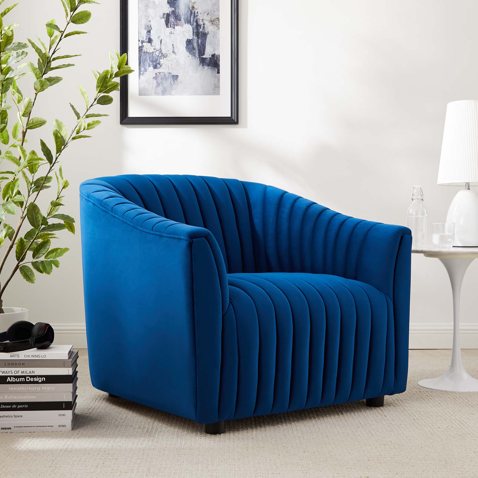 Three-quarter lifestyle view of the structured navy velvet barrel armchair styled in a minimalist room next to a modern white tulip side table and lamp.