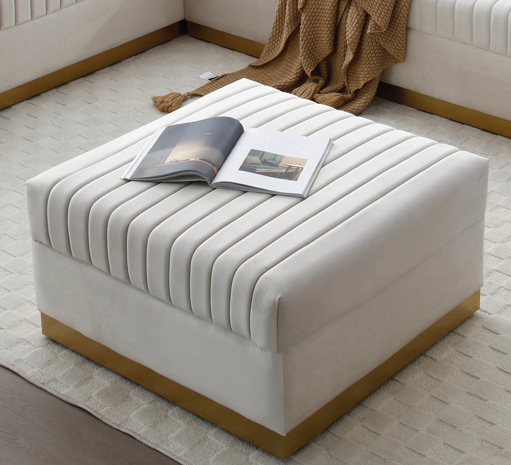 High-end living room setting featuring the cream velvet square ottoman styled on a textured rug with an open book on top beside a modern sectional sofa.