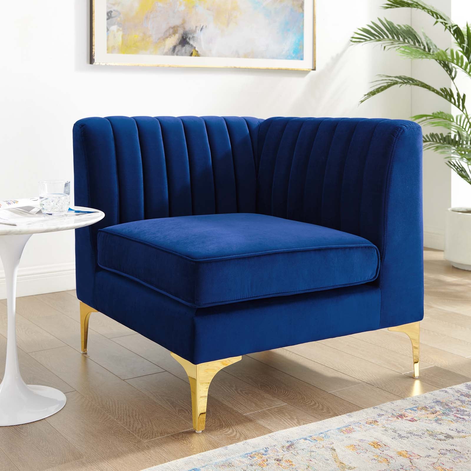 Navy velvet corner chair styled beside a marble side table and potted palm in a bright living room