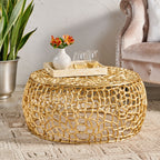 Gold mesh coffee table styled beside a velvet armchair, topped with a tray, vase, and stemware