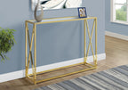 Gold X-frame glass console table styled against a blue wall with a vase, framed photo, and abstract art above