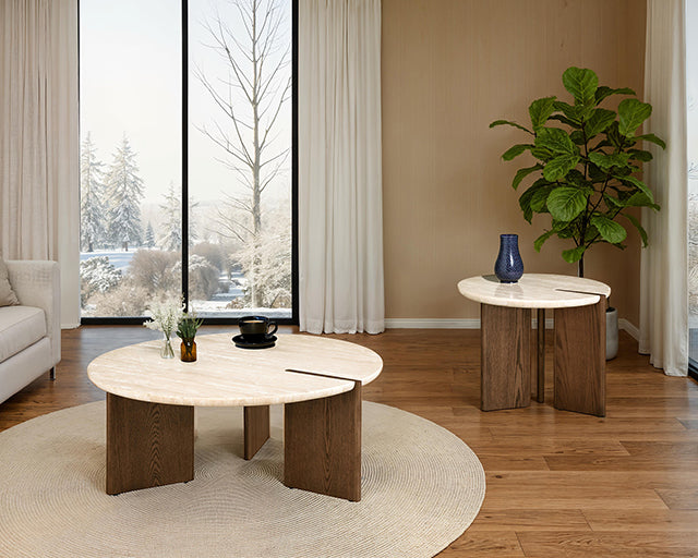 Travertine side table and matching round coffee table with ash tripod bases styled in a living room with a snowy window view