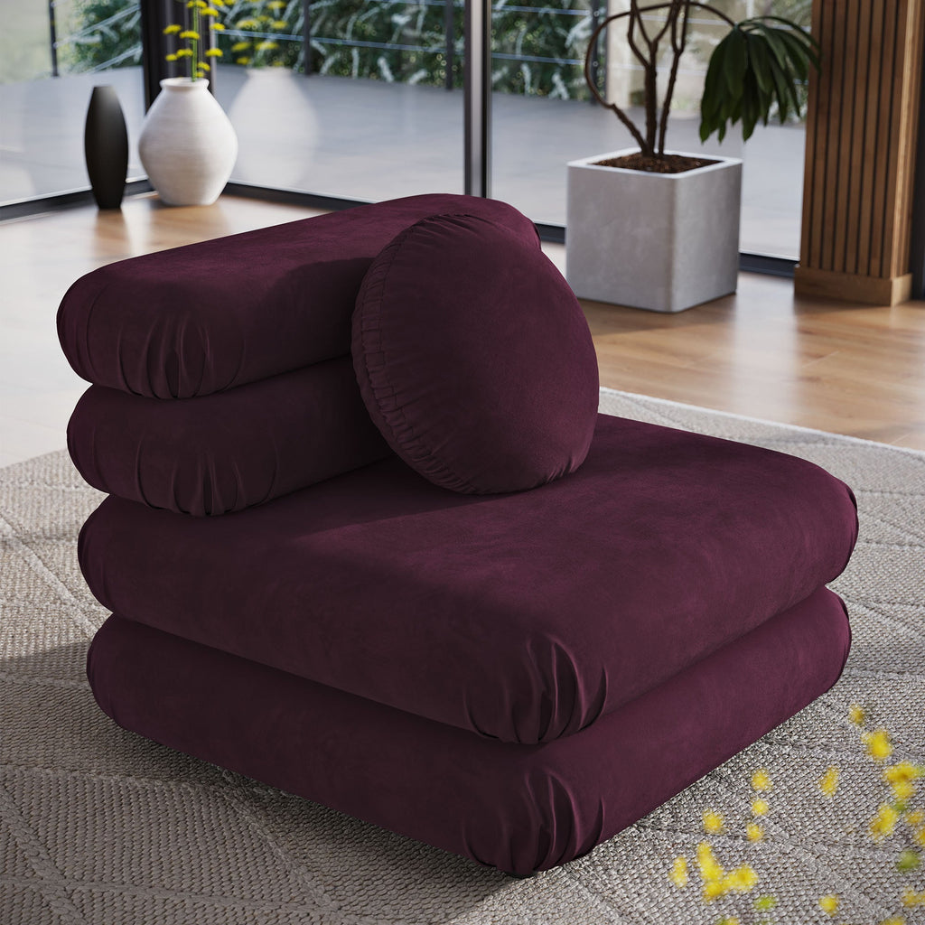 Deep plum velvet armless chair styled on a woven rug near floor-to-ceiling windows with potted greenery