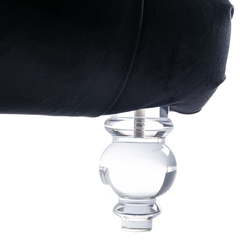 Close-up of the Rochelle Chaise's faceted, crystal-clear acrylic foot beneath black velvet upholstery