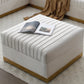 Ivory velvet ottoman with gold base styled with an open magazine and knit throw beside a sectional sofa