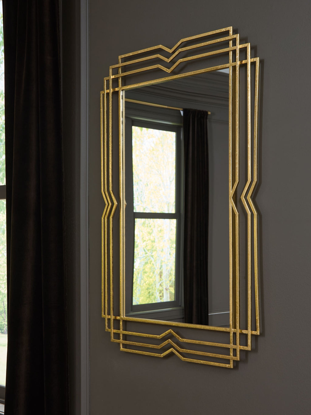 Gold layered-frame mirror hung on a dark charcoal wall beside a curtained window